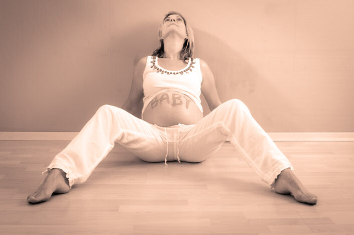 Junge Schwangere mit Babybauch sitzt auf dem Boden